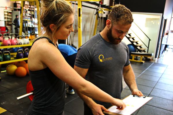 Personal trainer for beginners at 5th Element Wellness in Fitzroy North reviewing a personalised four-week beginner gym program and strength training plan with a client.