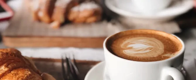 A coffee and croissant on a table with utensils, symbolizing a typical breakfast that may lead to energy crashes.