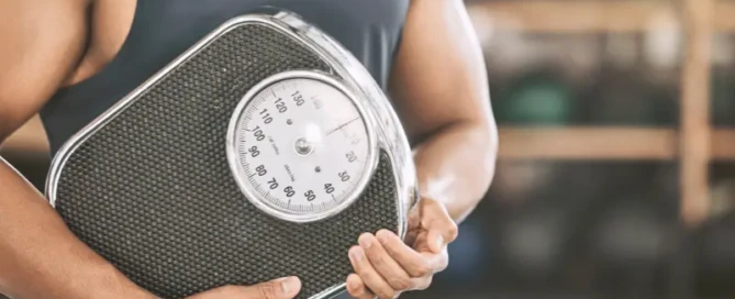 Man holding a weighing scale, representing the hidden impact of visceral fat on health and fitness.
