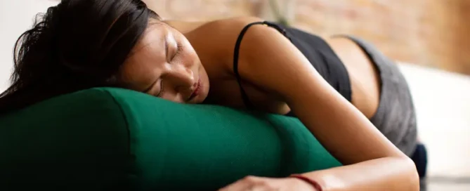 Woman sleeping on a yoga mat with her head on a pillow, symbolizing rest and recovery for better fitness results.