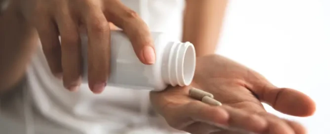 Woman dropping capsules from a bottle into her palm, representing magnesium supplementation for improved energy, recovery, and sleep.