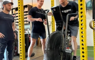 Coaches guiding a client on a bike mill during a personal training session