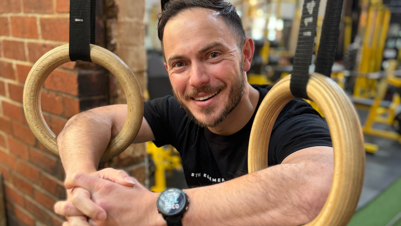 Sam Roberts smiling and leaning on gymnastic rings at 5th Element Wellness in Fitzroy North, promoting holistic coaching services