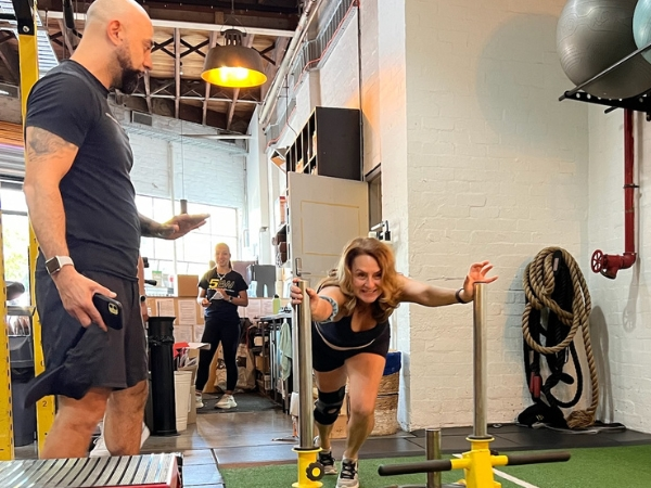 Personal training for adults over 40 at 5th Element Wellness in Fitzroy North, showing a coach guiding a woman through a controlled sled push focused on joint safety and posture.