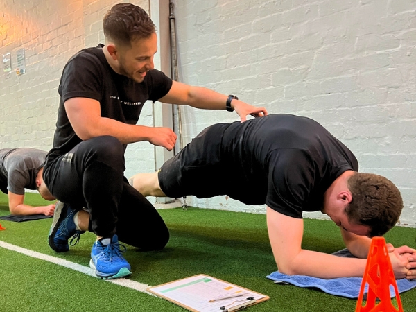 Personal training for adults over 40 at 5th Element Wellness in Fitzroy North, showing a coach assisting a client in a supported elbow plank during a strength and stability assessment.