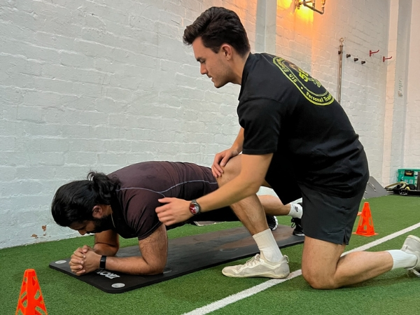 PT for busy adults at 5th Element Wellness in Fitzroy North, showing a personal trainer supervising an elbow plank to build core strength, posture, and resilience.