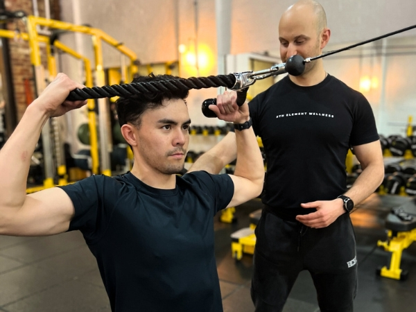 Personal training for busy professionals at 5th Element Wellness in Fitzroy North, showing a coach supervising a client performing a cable face pull with controlled technique.