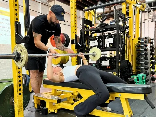 Trainer spotting a client during a barbell bench press session inside 5th Element Wellness in Fitzroy North