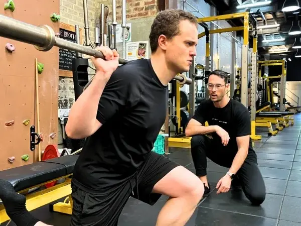 Coach giving technique cues while a client performs a barbell split squat at 5th Element Wellness.