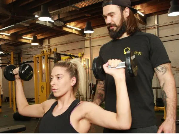 Woman doing dumbbell shoulder press exercise with male personal trainer in gym