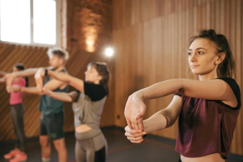 Group of people performing warm-up stretches during fitness class indoors