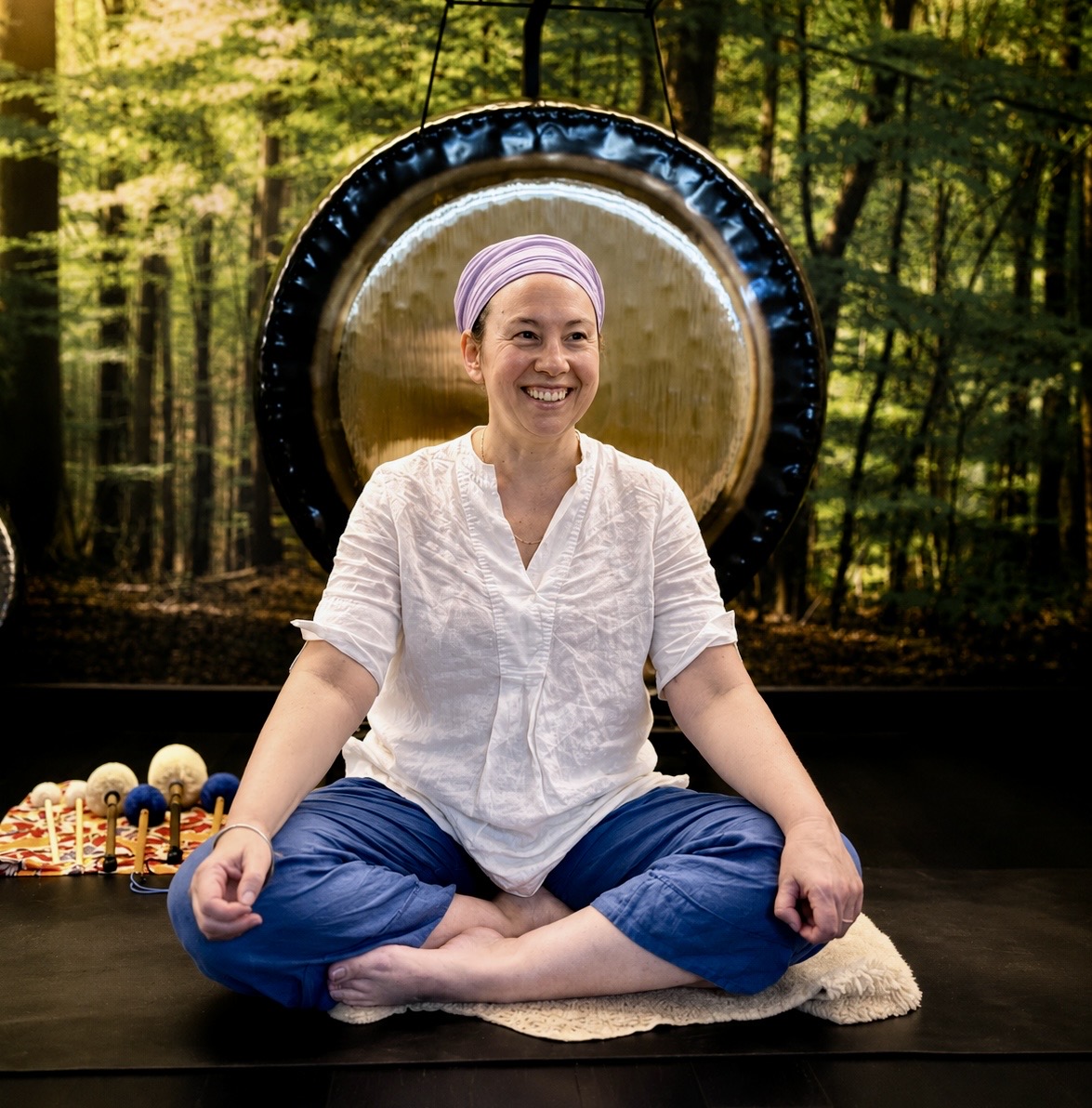 Female yoga teacher in front of a gong with a feature wallpaper green nature background